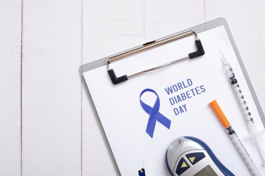 Text World Diabetes Day and blue ribbon on tablet with glucometer and syringes on a wooden background, top view. High quality photo