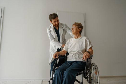 Professional male doctor carrying patient on wheelchair in medicine clinic hall. High quality photo