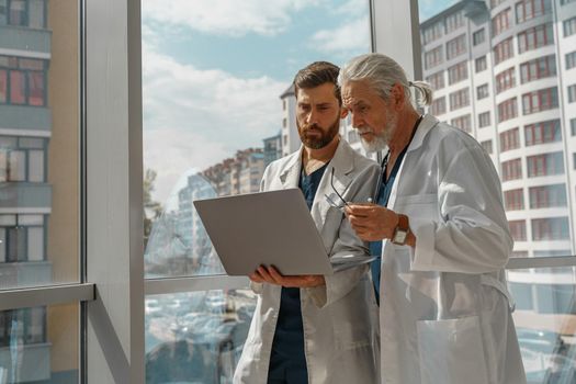 Two doctor colleagues discussing patient diagnosis stand in medicine clinic near panoramic windows