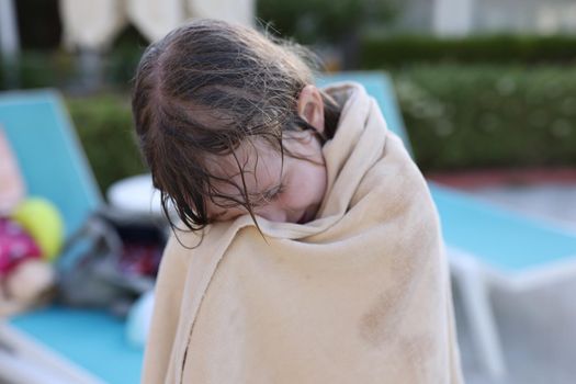 Girl child is wrapped in warm beach towel. Summer children recreation and hypothermia on water