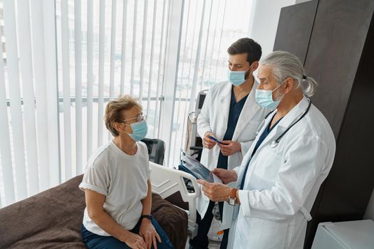 Doctors in masks explain to a sick patient in a wheelchair her diagnosis . High quality photo