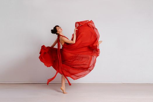 Dancer in a red flying dress. Woman ballerina dancing on a white studio background.