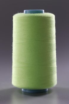 Light green spool of thread on gray background. Sewing machine materials and high-quality durable threads