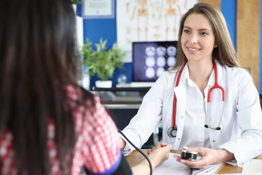 Beautiful female doctor working with patient measures blood pressure. Doctor uses tonometer to measure blood pressure of young woman and takes notes