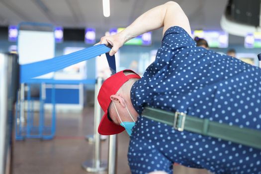 Man in a protective mask raises access tape and goes to registration without queue. Violation of rules of medical and passport control in public places airport station
