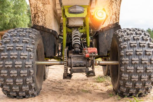 Rear view of the ATV standing on sandy ground. Wheels and suspension of the all-terrain vehicle. The concept of travel and adventure. shock absorbers, brakes, exhaust pipe, axles, chain, gear