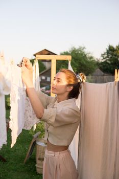 Laundry day. A woman hangs linen and towels on a tree in the courtyard of a village house. Summer cottage concept.