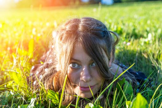 the face of a girl lying in the grass close-up. summer outdoor recreation. relaxation. portrait of a beautiful young teenage girl lying on the grass in the park and smiling and looking at the camera. High quality photo