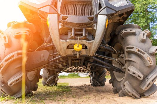 Front and bottom view of the ATV standing on sandy ground. Wheels and suspension of the all-terrain vehicle. The concept of travel and adventure. shock absorbers, brakes, axles, winch, hinges, wheels and headlights, bottom protection