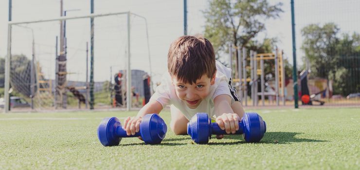 A child with dumbbells on the playground. A sporty kid. Illustrating an article about sports. Children's exercises. Education of champions. Light weightlifting. Lifestyle