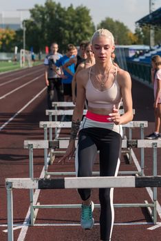 Young woman athlete runnner is exercising hurdles at the stadium outdoors