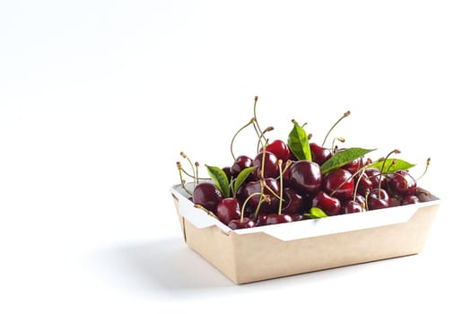 Fresh, ripe cherries in a cardboard box on a white background. Copy space