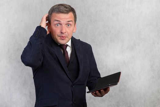 Portrait of a strange surprised man in a blue jacket on a white background holds an electronic gadget in his hand. Man on a white isolated background.