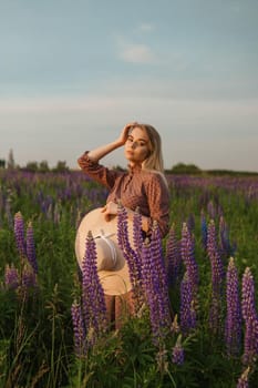 A beautiful woman in a straw hat walks in a field with purple flowers. A walk in nature in the lupin field.