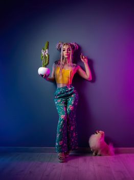 the stylish girl with dreadlocks in fashionable bright clothes on a neon background with a small pomeranian dog
