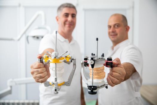 Two male dentists holding dental articulators in a dental clinic