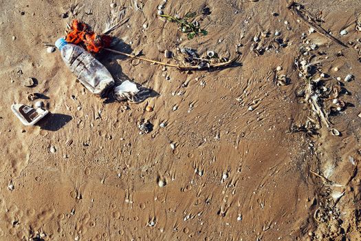 background of a plastic bottle and trash on the sand of the beach polluting the sea and the marine life, concept of pollution control of the oceans by plastic