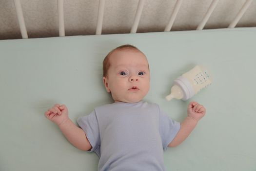 Baby with a bottle in the crib top view . Baby food copyspace . Children's food. Hungry baby. Infant formula .