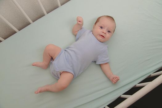 The baby is lying in his crib and looking at the camera . Happy baby. Happy childhood. Kid top view
