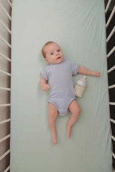 Baby with a bottle in the crib top view . Baby food copyspace . Children's food. Hungry baby. Infant formula .
