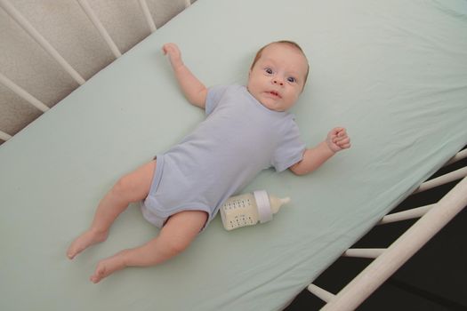 Baby with a bottle in the crib top view . Baby food copyspace . Children's food. Hungry baby. Infant formula .