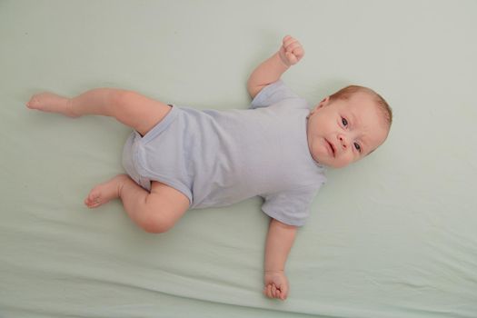 The baby is lying in his crib and looking at the camera . Happy baby. Happy childhood. Kid top view