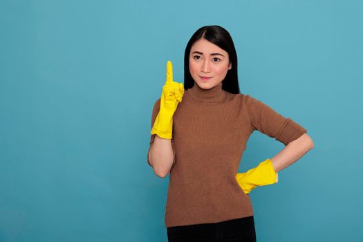 Smiling satisfied delighted asian houseworker wearing yellow gloves and pointing finger upward to copy space, Cleaning home concept, Glade optimistic and positive housemaid