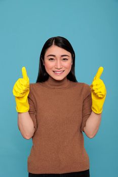 Excited happy and cheerful maid from housework thumbs up and wearing yellow gloves for hand safety isolated on a blue background, Cleaning home concept, Satisfied glade female with positive mood