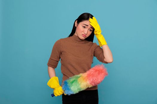 Sad depressed and overwhelmed asian housemaid tired from chores holding colorful duster brush in yellow glove Cleaning home concept, Houseworker feeling exhausted unhappy and negative from work