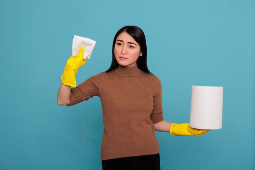 Confidence young woman with tissue paper holding in the yellow glove standing against a blue background, Cleaning home concept, Faithful satisfied female from day to day chores