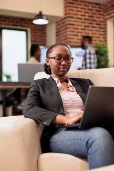 African american project manager analyzing data on laptop, using online research information to create business report. Browsing internet website to work on company management, startup office.