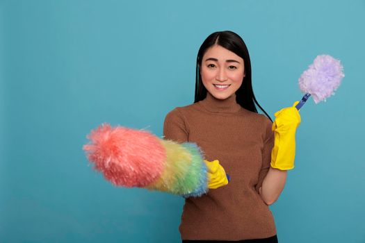 Laughing glad and smiling asian young housekeeper from chores holding two duster brush in yellow gloves, Cleaning home concept, Woman feeling positive from day to day work