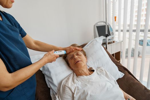 Doctor measures patient's temperature with non-contact thermometer during treatment in hospital ward