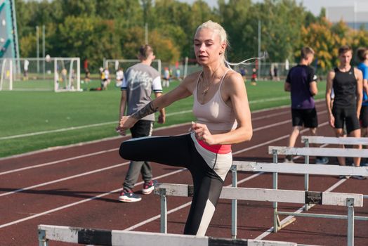 Young woman athlete runnner is exercising hurdles at the stadium outdoors