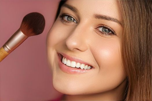 Beautiful young woman applying cosmetic powder product with make-up bamboo brush, beauty, makeup and skincare cosmetics model face portrait on pink background, closeup