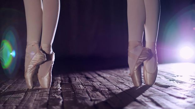 close up, in rays of spotlight, on the stage of the old theater hall. ballerinas standing on toes in pointe shoes, performs elegantly a certain ballet exercise, pas de bourre suivi. High quality photo