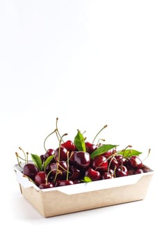 Fresh, ripe cherries in a cardboard box on a white background. Copy space. Vertical photo