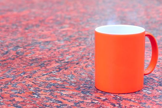 a small bowl-shaped container for drinking from, typically having a handle. Red ceramic cup mug on bright red blue spotted background.