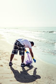 man collecting waste that pollute the sea in plastic bag, people helping to keep nature clean and picking up the garbage from shore, volunteer campaign to cleaning on the beach, vertical photo