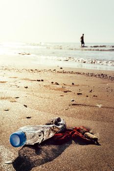 vertical photo of a plastic bottle and garbage lying on the shore of the beach polluting the sea and the marine life, concept of pollution control of the oceans by plastic