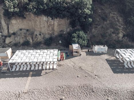 Empty sun loungers under a canopy on the beach. The beach area is empty. No people. White plastic sunbeds under the sun shade. The holiday season ends. Holiday season begins. Waiting for tourists