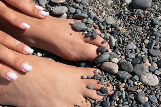 Women's hands and feet on the background of a rocky beach of sea pebbles.