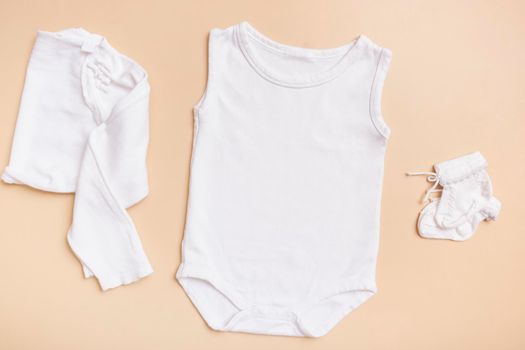 White baby bodysuit mockup for logo, text or design on beige background with clothes top view.