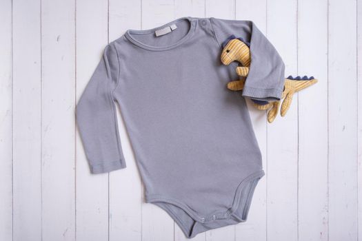 Grey baby bodysuit top view. Mock up for logo, text or design on wooden background. Flat lay with dinosaur.