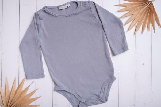 Grey baby bodysuit top view. Mock up for logo, text or design on wooden background. Flat lay with palm leaves.