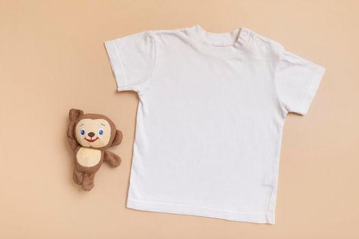 White baby t-shirt top view. Mock-up for logo, text or design on beige background. Flat lay child clothes with toy.