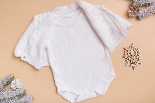 White baby bodysuit mockup for logo, text or design on beige background with winter decotations top view.