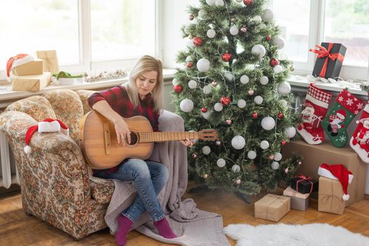 young woman holds a guitar in hand and sits in christmas studio.