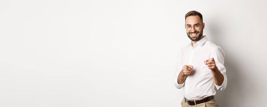 Confident businessman smiling, pointing fingers at you, congrats or praise gesture, standing over white background.