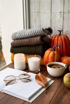 Hello fall. Cozy warm image. High angle view opened blank book for mockup design with sweaters and candles